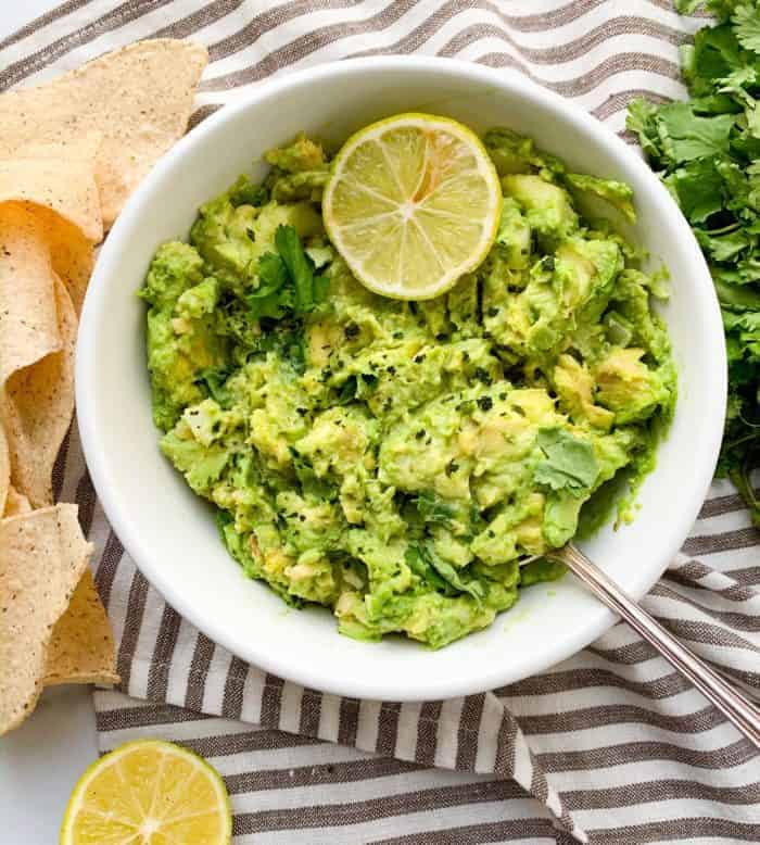 A white bowl filled with guacamole on a gray and white striped towel.