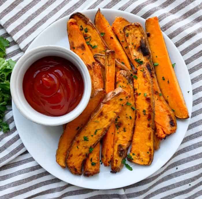 A white plate topped with sweet potatoes and ketchup,