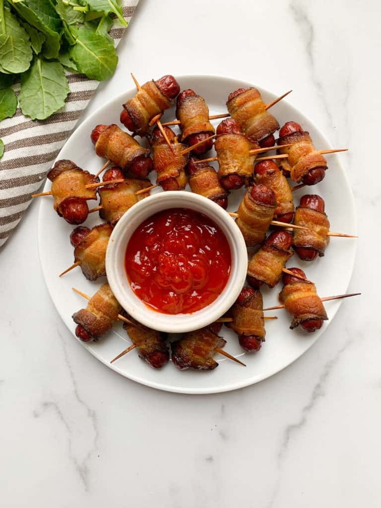 A white plate topped with mini hot dogs and ketchup.