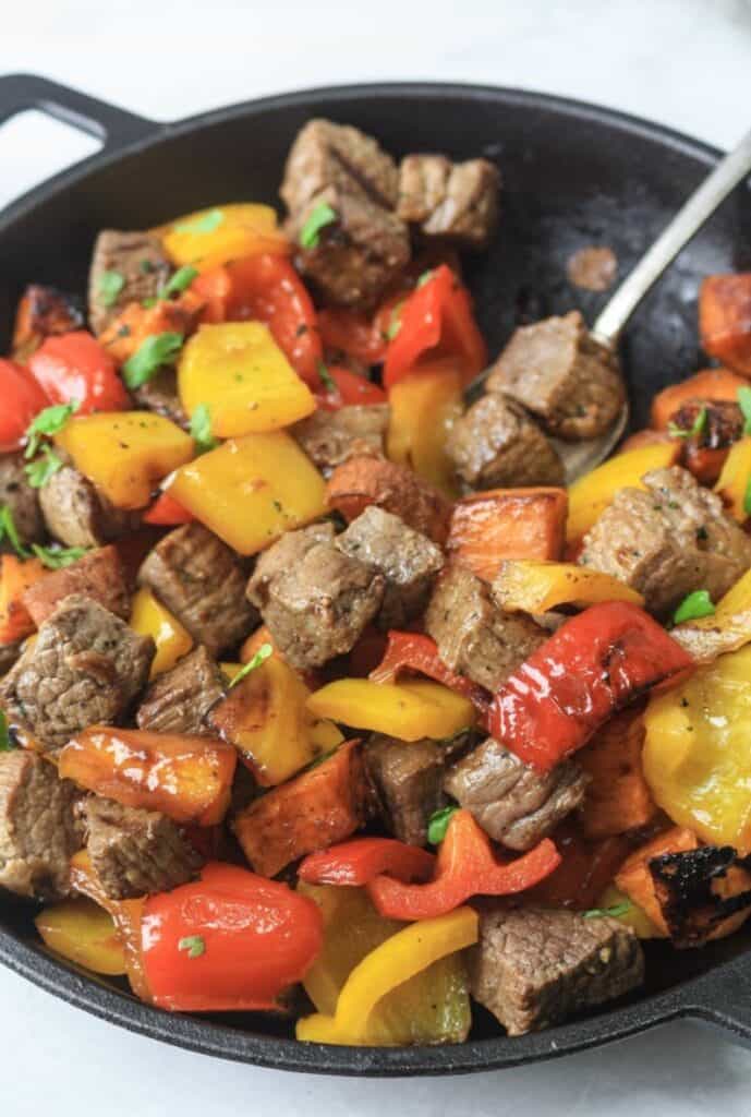 Whole30 steak bites with potatoes and peppers in a cast iron skillet.