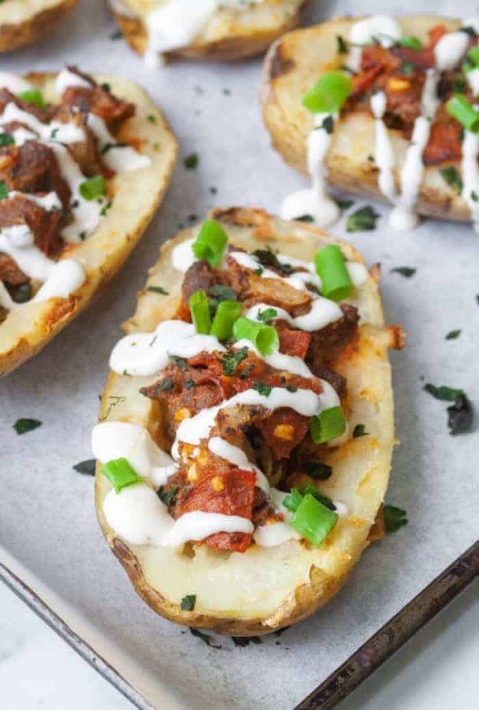 Sweet potato skins filled with tomatoes, pepperoni and marinara sauce on a baking sheet.