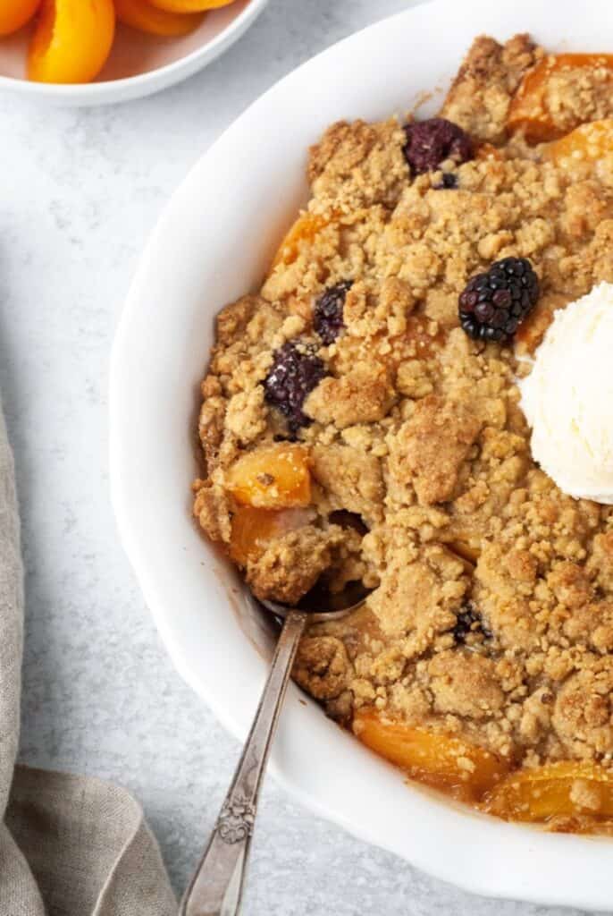 Paleo fruit cobbler with apricots and blackberries in a white pie dish.