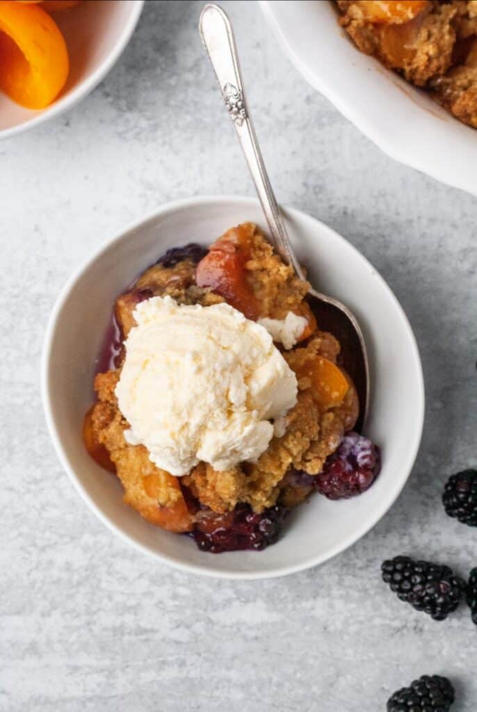 Paleo Fruit cobbler with apricots and blackberries in a white bowl with ice cream.