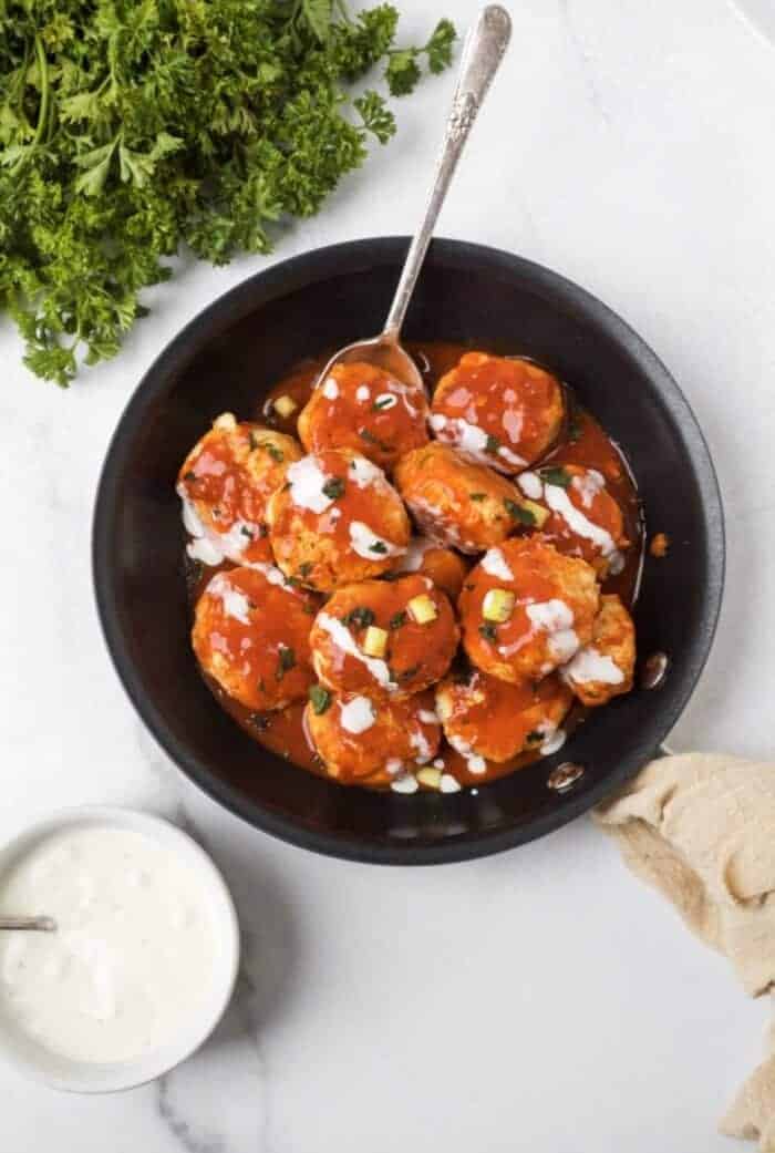 A black skillet filled with buffalo chicken meatballs and a ramekin of ranch dressing.