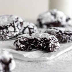 Chocolate cookies rolled in white confectioner's sugar on a piece of parchment paper.