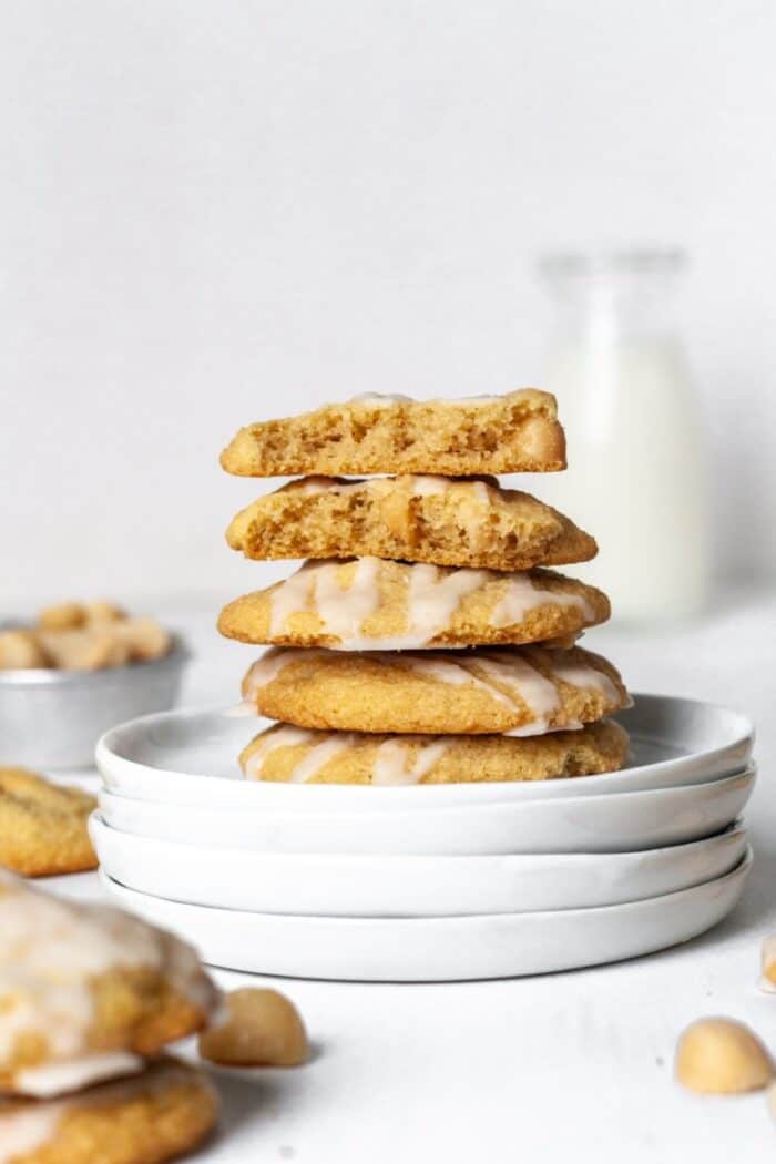 A stack of macadamia nut cookies on a white plate with a glass of milk in the background.