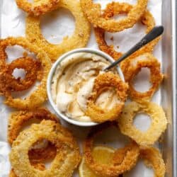 Onion rings on a baking pan with parchment paper and a garlic dip.