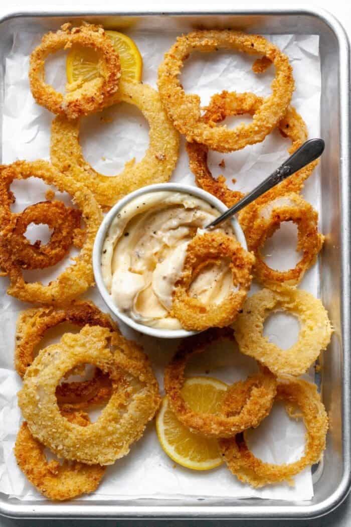 Onion rings on a baking pan with parchment paper and a garlic dip.