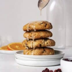 A stack of 4 almond flour orange cranberry cookies on a white plate with an orange glaze drizzled on top.
