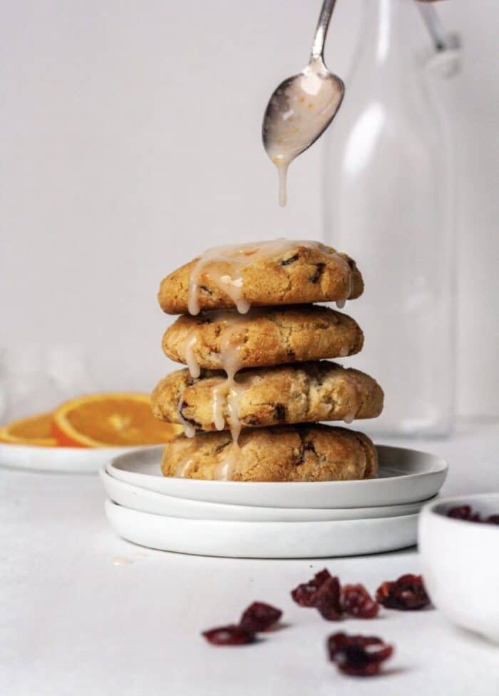 A stack of 4 almond flour orange cranberry cookies on a white plate with an orange glaze drizzled on top.