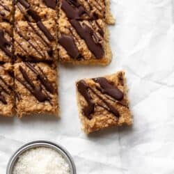 Samoa bars on white parchment paper with a measuring cup filled with coconut flakes.