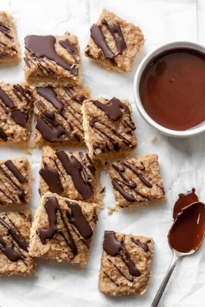 Samoa bars on white parchment paper with a bowl of melted chocolate.