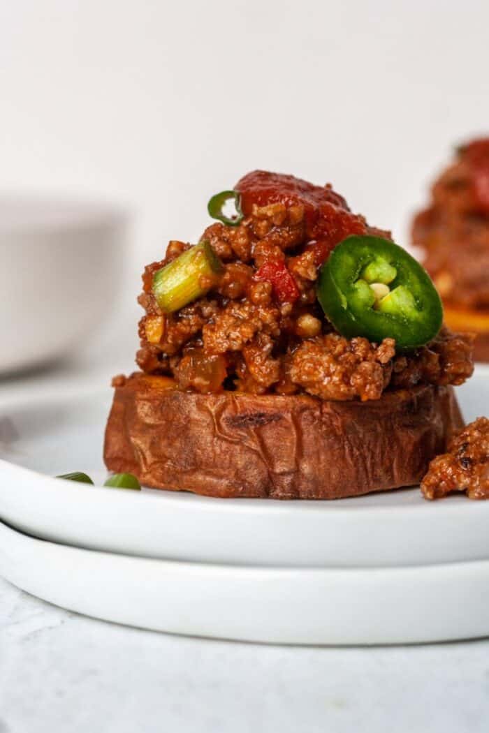 Sloppy Joes on top of a roasted sweet potato on a white plate.