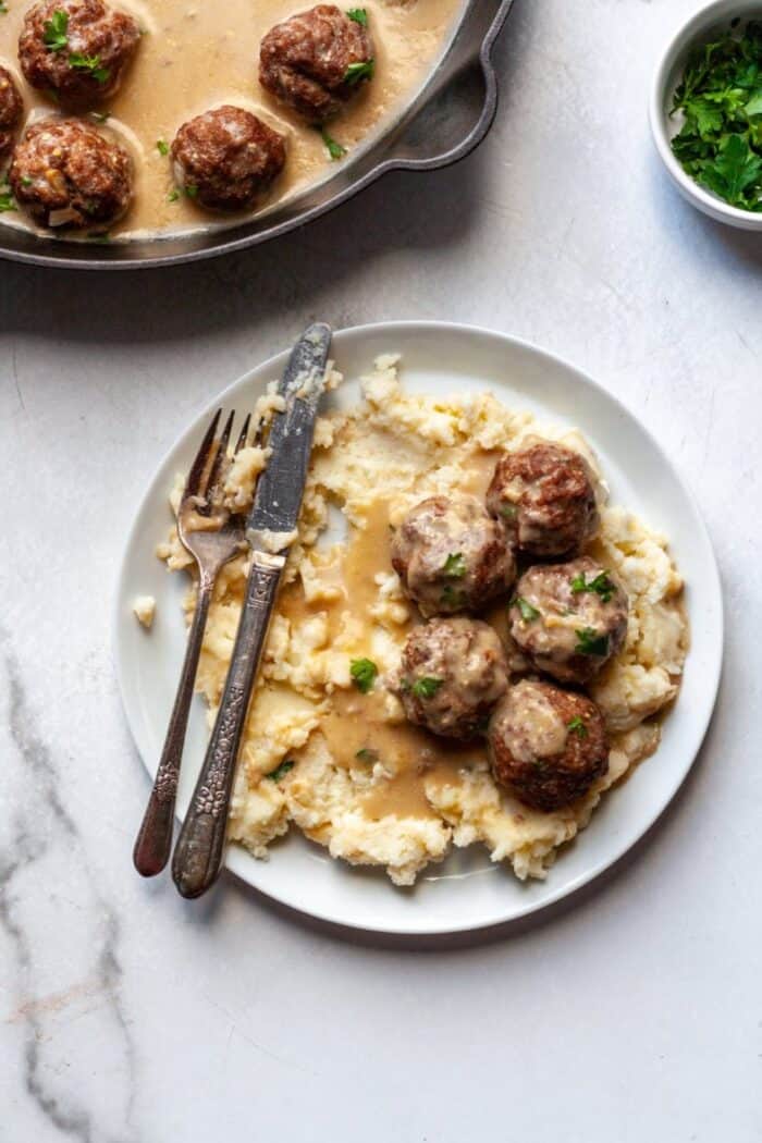 A white plate with mashed potatoes and meatballs.