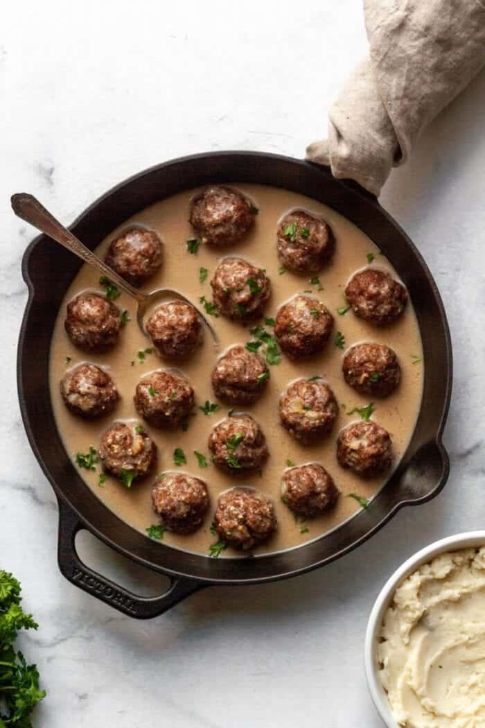 A black cast iron skillet filled with meatballs and gravy.