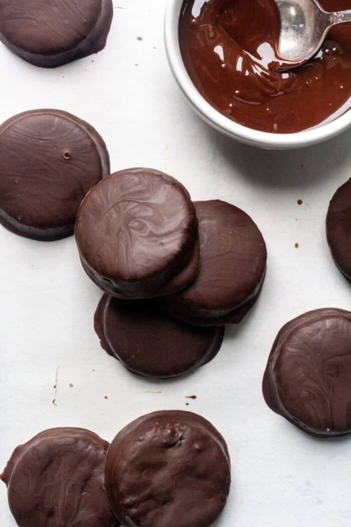Thin Mint cookies on a piece of parchment paper with a bowl of melted chocolate.