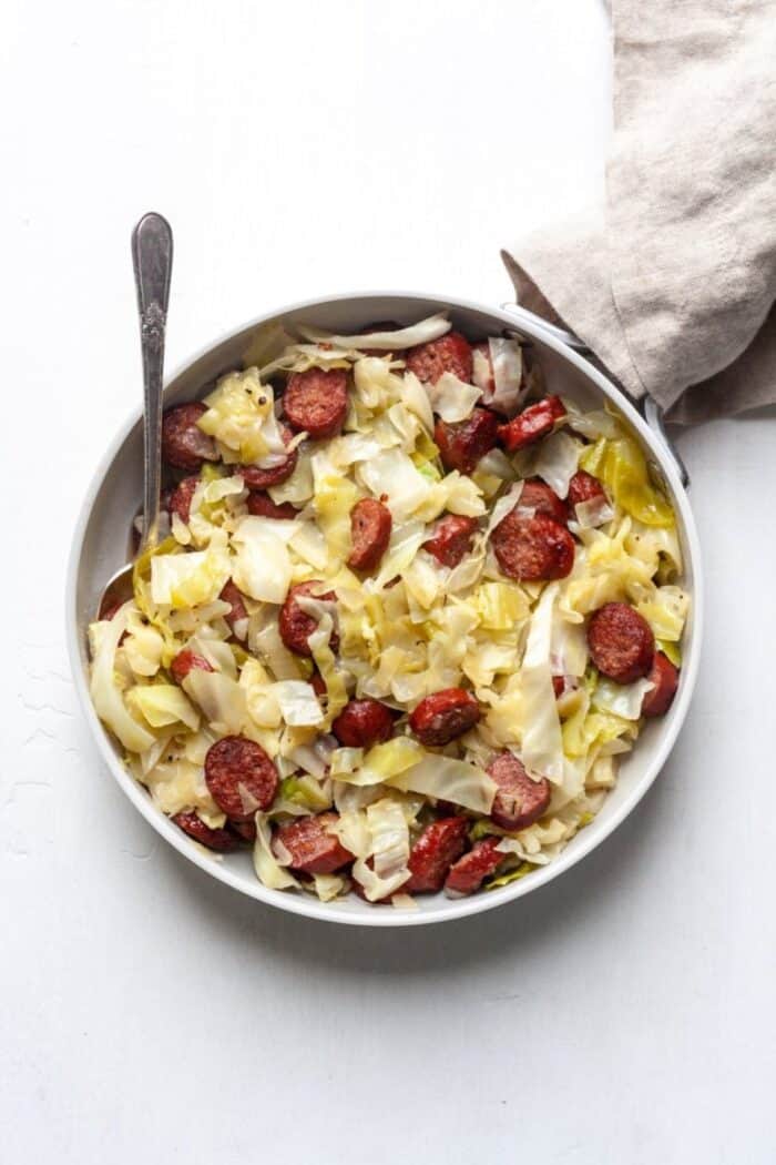 Paleo Braised Cabbage and Sausage in a white skillet.