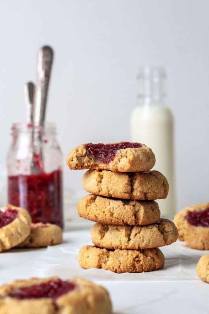 Vegan thumbprint cookies on a white backdrop with raspberry jam.