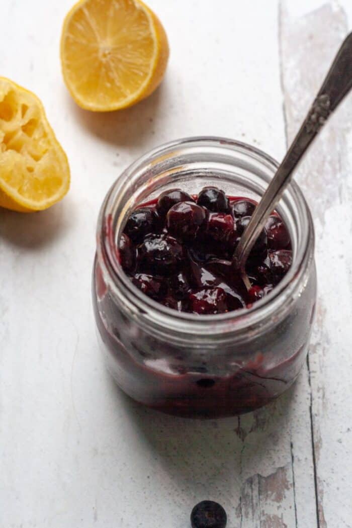 A jar filled with Vegan blueberry jam and lemon slices.