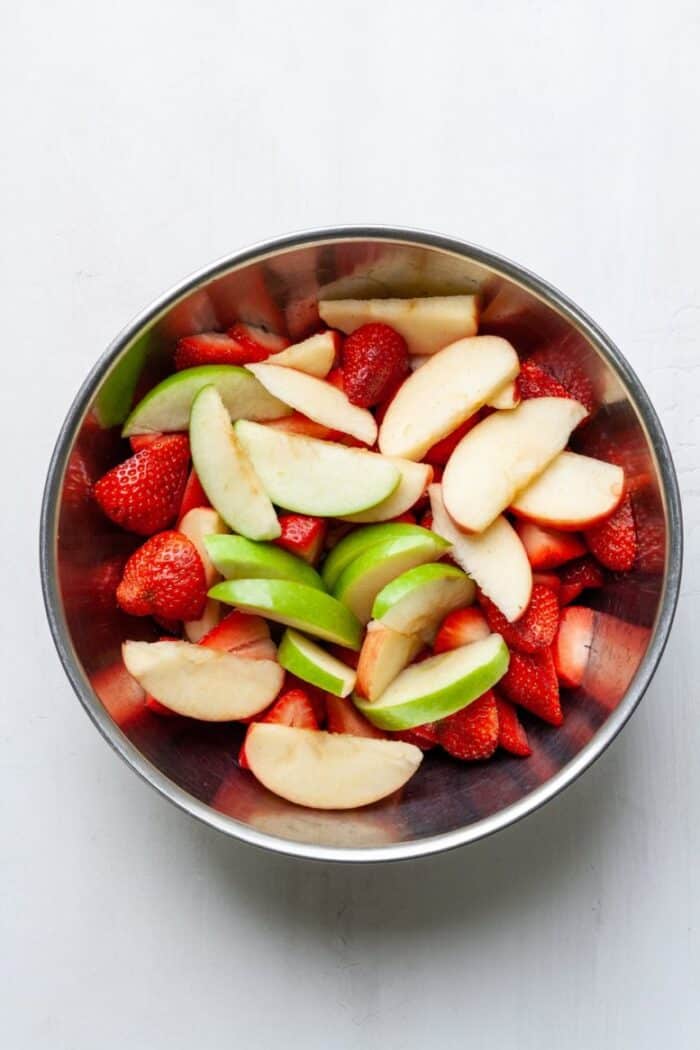 A bowl filled with sliced strawberries and apples.