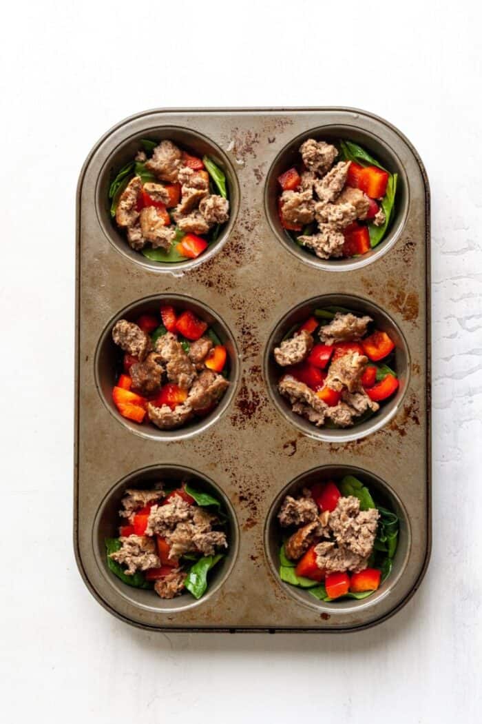 A muffin tray with sausage and veggies.