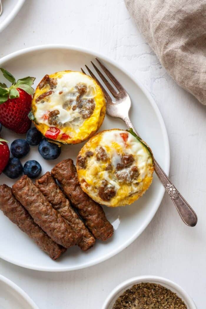 Whole30 Egg muffins on a white plate with air fryer sausage and fruit.