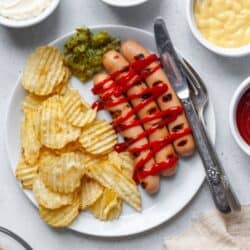 Hot dogs on white plate with ketchup and chips