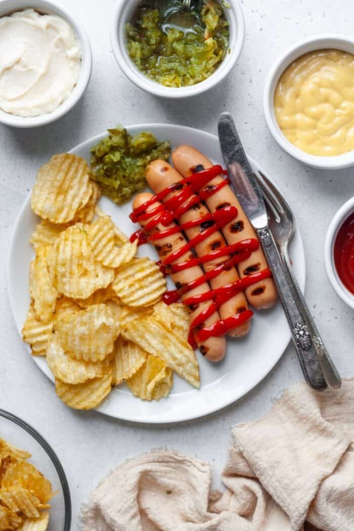 Hot dogs on white plate with ketchup and chips
