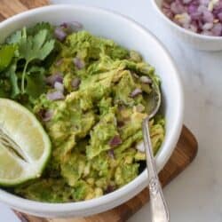 Bowl of guacamole with cilantro, onions and lime