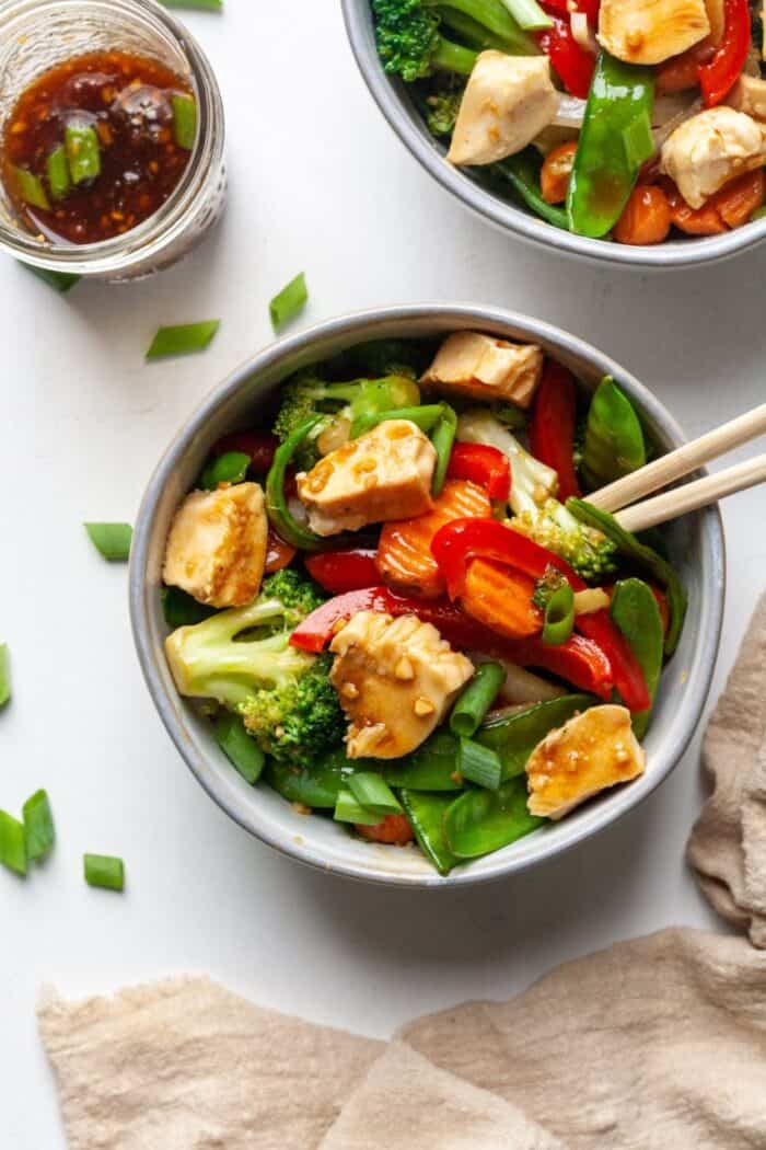 Chicken and veggie stir fry in bowl with chopsticks