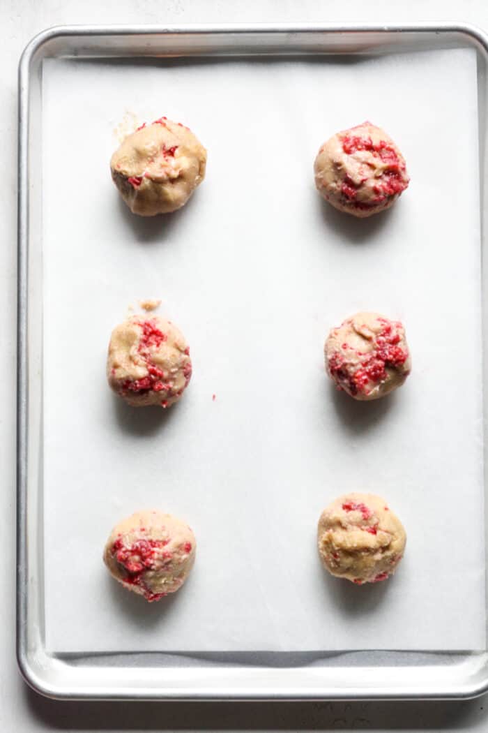 Thick balls of raspberry cheesecake cookie dough on pan