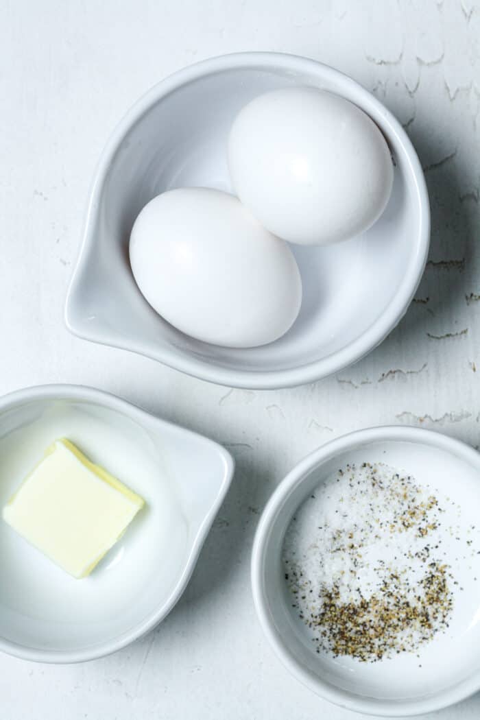 Eggs, butter, salt and pepper in small white bowls