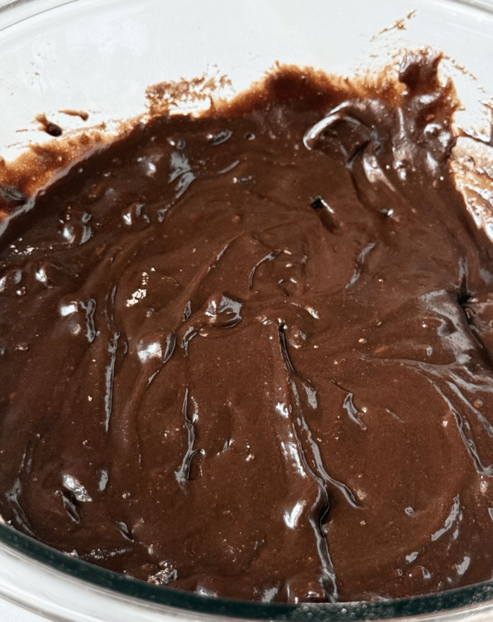 Thick brownie batter in glass bowl.